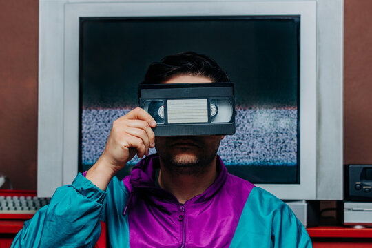 Man in retro 80s jacket holding VHS tape over face, TV static backgroun