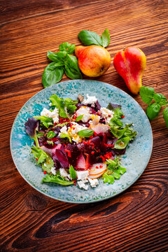 Vegetarian vegetable and fruit salad with red beets, pear, greens and feta sheep milk cheese served as close-up on a design plate