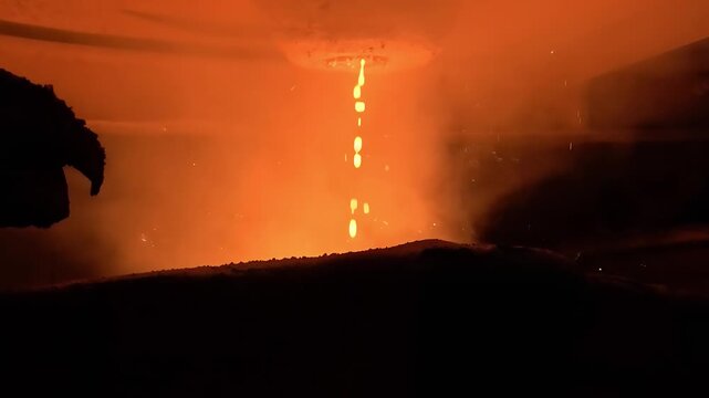 Molten Metal Pouring From Overhead Vessel in Dark Foundry With Sparks