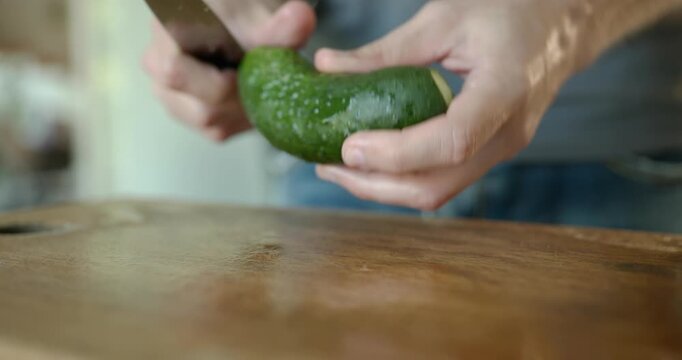 Close-up male hand cut cucumber with knife on wooden cutting board. 4K 10-bit