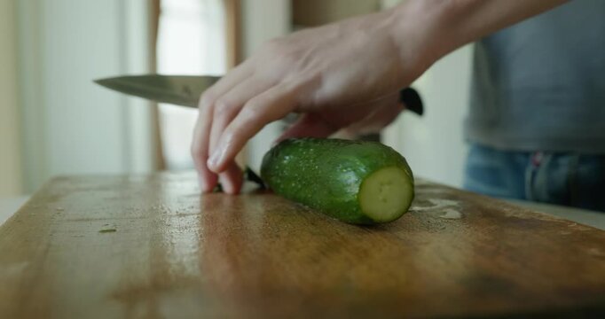 Close-up male hand cut cucumber with knife on wooden cutting board. 4K 10-bit