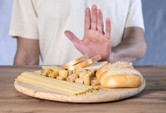Gluten allergy,  young man hand push out, refusing to eat breads slice and pasta on chopping board in food meal at home, man having a stomach ache. Gluten intolerant and Gluten free diet concept.
