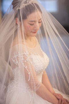  Portrait of elegant Asian bride in lace wedding dress and veil, soft natural window light, bridal morning preparation
