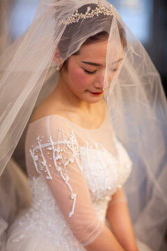  Portrait of elegant Asian bride in lace wedding dress and veil, soft natural window light, bridal morning preparation