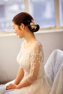 Beautiful Asian bride in white beaded wedding gown with tiara and veil, soft window light, wedding preparation portrait
