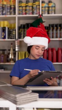 Hispanic female store clerk wearing a santa hat checking inventory using a digital tablet