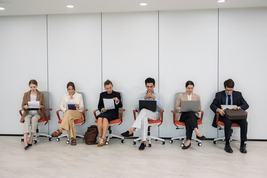 Group of diverse job applicants seated in an office waiting room before interviews, illustrating hiring, candidate assessment, career planning, and corporate recruitment.