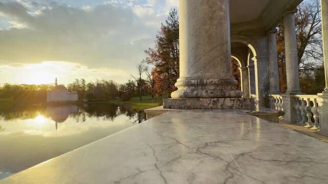 Marble columns frame a peaceful lake view with the Turkish Bath pavilion reflected at golden sunset. A quiet scene in Catherine Park, Pushkin, Russia brings warm serenity and wonder.