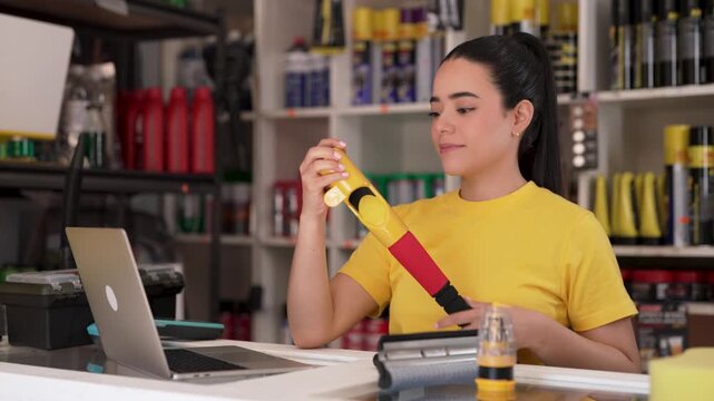 Female store clerk using laptop while checking car cleaning equipment at store counter