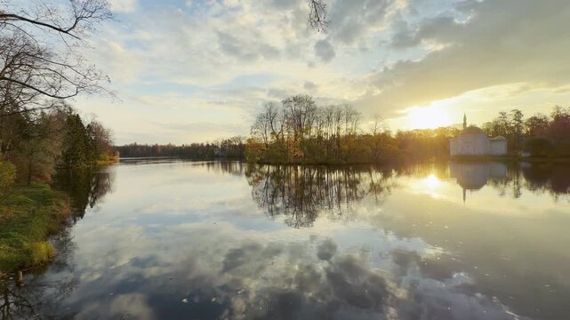 The Turkish Bath pavilion sits peacefully on the shoreline as golden sunlight glimmers over calm waters. A tranquil sunset in Catherine Park, Pushkin, Russia brings a feeling of quiet awe.