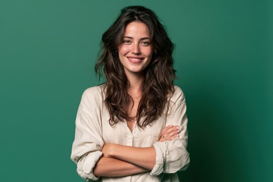 Portrait of a cheerful woman with wavy hair and folded arms against a vibrant emerald green backdrop