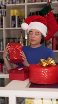 Cheerful latin retail clerk wearing a festive santa hat arranging wrapped gift boxes in store