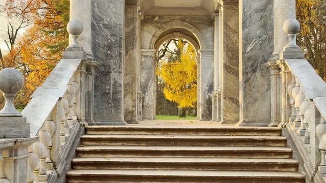 A marble staircase leads through elegant arches in Catherine Park, Pushkin, Russia, in slow motion. Bright golden autumn foliage frames the view, inspiring peaceful, majestic feelings.