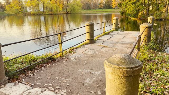 A stone pier leads toward the calm Great Pond in Catherine Park, Pushkin, Russia, in slow motion. The golden autumn sunlight creates peaceful, heartwarming emotions.
