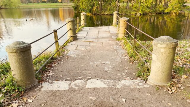 A stone pier extends toward the calm lake bordered by autumn trees. A peaceful slow motion movement in Catherine Park, Pushkin, Russia inspires quiet reflection and harmony.