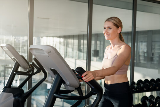 Smiling woman training on elliptical cross trainer machine at gym