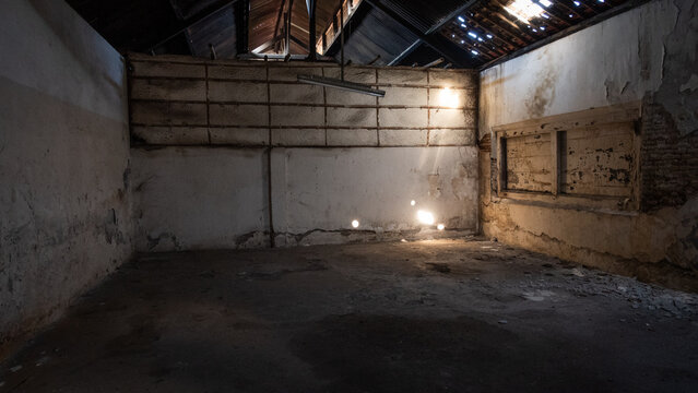 Abandoned building interior with cracked walls, peeling plaster, exposed roof beams, and debris on a concrete floor, depicting urban decay, derelict property, and neglect.