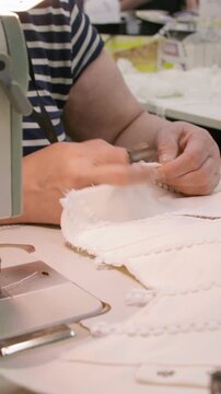 Vertical video. Tailoring occupation. Textile work. Woman hand clipping seam on white clothes with professional scissors. Seamstress workflow on desk.