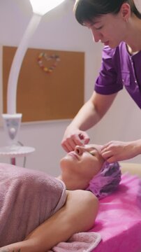 Vertical video. Skin relaxing. Detox procedure. Female professional cosmetologist preparing client for beauty treatment face care in aesthetic salon.