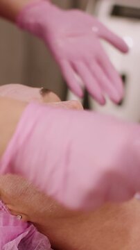 Vertical video. Clay mask. Therapy treatment. Cosmetologist hand using brush applying product on woman skin face in beauty salon for healthy procedure.