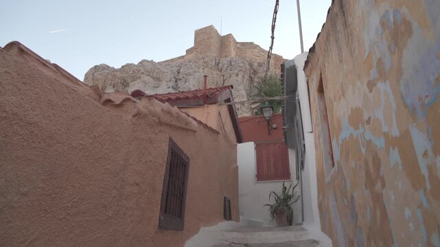 Weathered ochre and terracotta houses with small windows nestled beneath the rocky slope of the Acropolis in Anafiotika, Plaka, Athens, Greece.