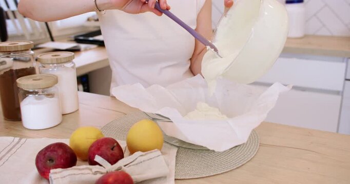 Preparing cheesecake. Baking food. Female confectioner hand pouring white cream liquid dough in bowl with spatula on parchment paper.