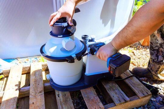 Worker works on setting up pool filter in backyard on sunny day while using power tools