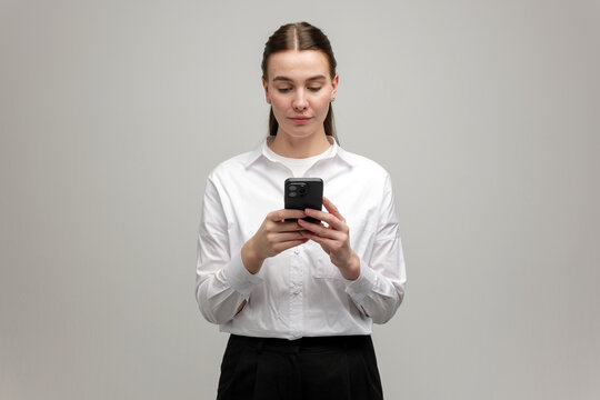 Focused young woman engaging with her smartphone against a neutral backdrop
