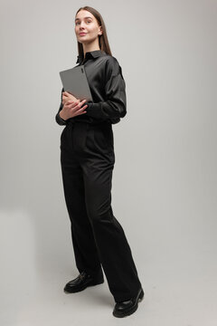 Modern businesswoman in stylish black attire holding a tablet while standing confidently indoors