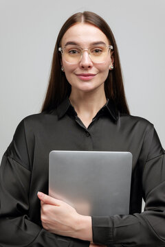 Young professional woman poses confidently holding a laptop in a modern indoor setting