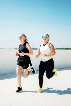 Two women jogging in sporty outfits under a clear blue sky