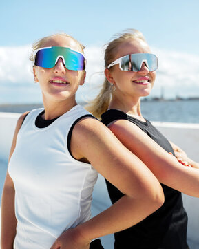 Two friends in stylish sunglasses pose confidently against a sunny waterfront backdrop