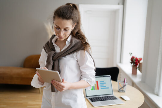 Young woman engages with tablet while standing in a bright home office space