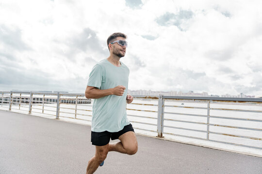 Running along the waterfront pathway on a cloudy day with determination and focus