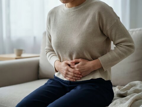 Woman sitting on a sofa and holding her stomach due to abdominal pain or discomfort