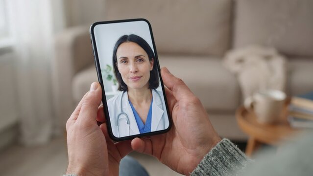 Person holding a smartphone during a telehealth video call with a female doctor