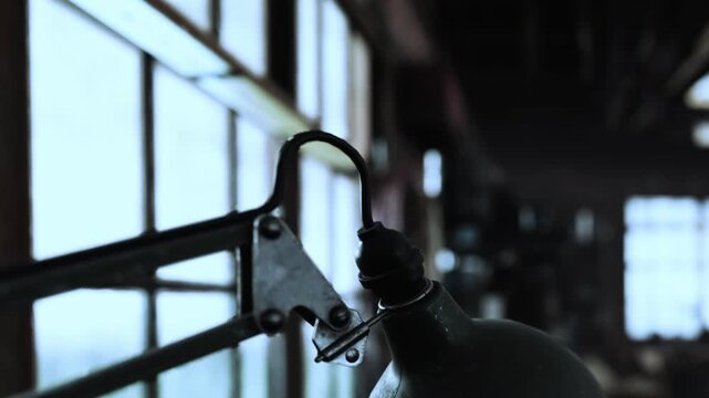 Old metal lamp arm and joint mechanism stands near large window providing soft natural light inside