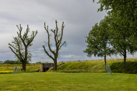Wide angle coastal digital publication of historical brick bunker dike embankment pollard trees green lawn Veere Zeeland Netherlands European travel defense heritage commercial