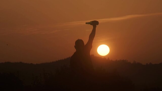 Man pouring traditional asturian cider from a bottle at sunrise, celebrating summer solstice against a golden morning sky