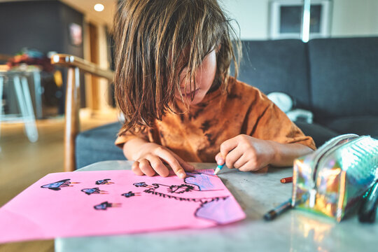 Boy Coloring Artwork on Pink Paper with a Pencil Case Nearby