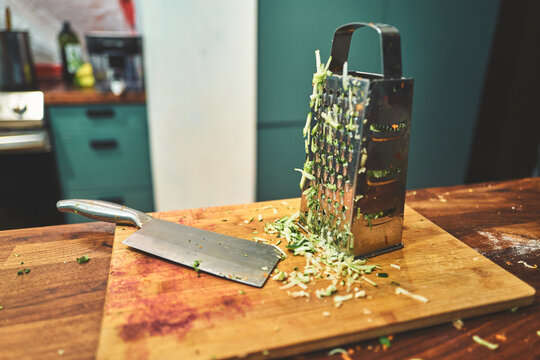 Box Grater with Shredded Zucchini and a Cleaver on a Cutting Board