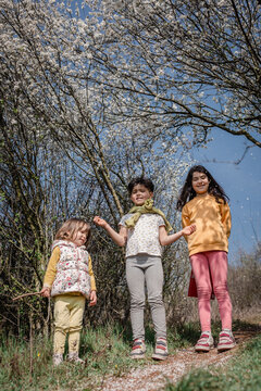 Three Sisters Smiling Beneath Blossoming Spring Trees in a Sunny Garden