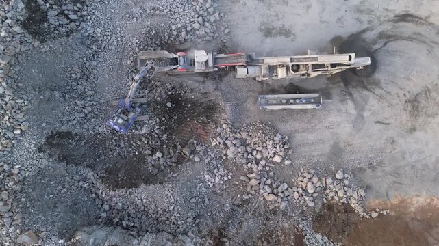 Espoo, Finland-April 14, 2025: Aerial perspective revealing powerful excavator loading fragmented rocks into mobile crusher at sunlit Finnish quarry during springtime industrial operations