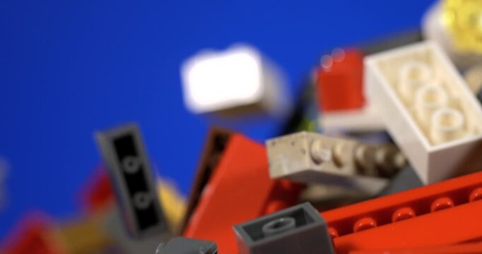 Slow motion Colorful construction toy pieces fill frame against blue background. Small plastic building elements include red, gray, white and tan bricks, with varied shapes and connecting studs.