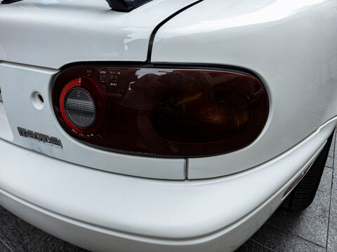 GANDIA, SPAIN - OCTOBER 4, 2026: Rear tinted taillight and Mazda emblem on a classic white first-generation Mazda MX-5 Miata roadster.