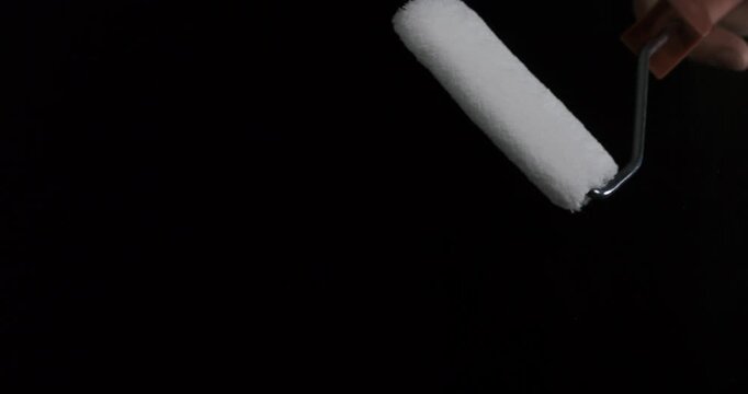 Interior decorator lifts paint roller against black background with care. White nap roller and metal frame stay poised for interior wall painting, while decorator keeps tool clear of visible surfaces.