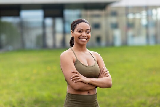 Smiling Young African American Woman Standing Confidently With Arms Crossed In Park During Daylight, Emphasizing Fitness And Wellbeing, Enjoying Outdoor Exercise In Natural Environment.