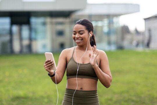 Smiling Black Female Runner Listening To Music On Smartphone While Jogging Outdoors In Green Park. Displaying Joy And Active Lifestyle In Nature. Weight Loss Concept.