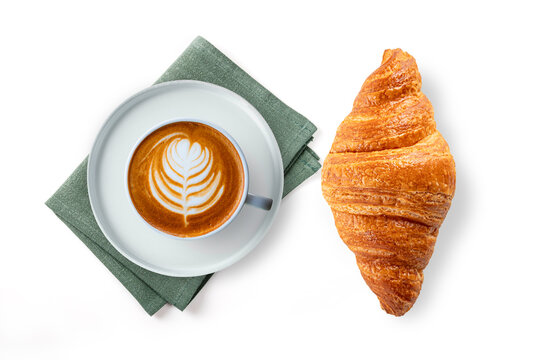 Cup of hot cafe latte with beautiful foam art and fresh golden croissant. Professional food photography isolated on white background. Top view