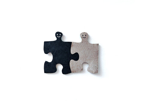 Two interlocking puzzle pieces with smiling faces symbolizing human connection, compatibility, relationships, teamwork, and belonging on a white background.